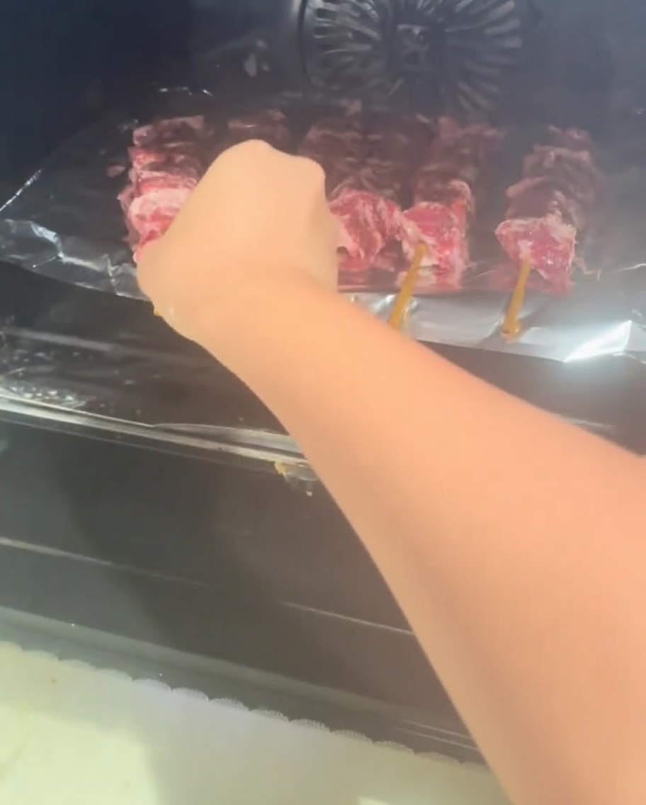 Ein Backblech mit rohen Rindfleischspießen wird in den Ofen geschoben.
