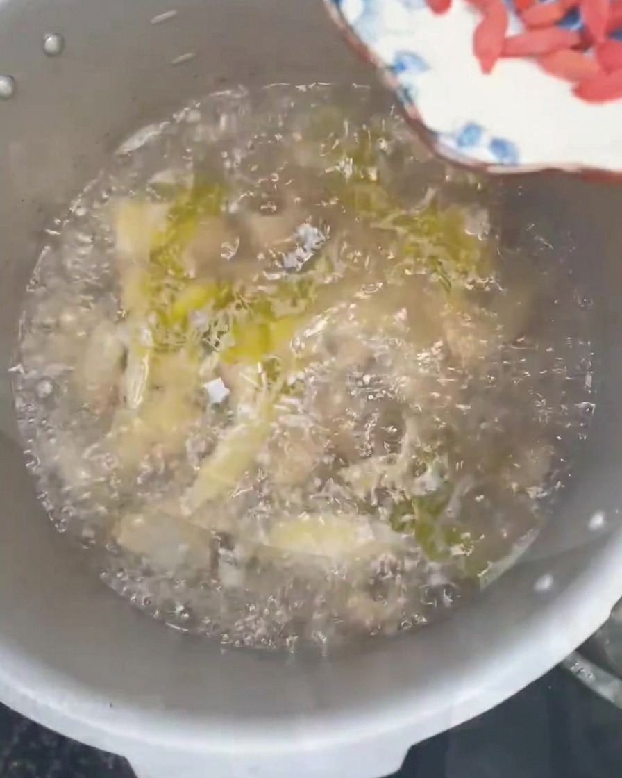 Goji-Beeren und frische gehackte grüne Frühlingszwiebeln werden in eine dampfende Hühnersuppe gestreut.