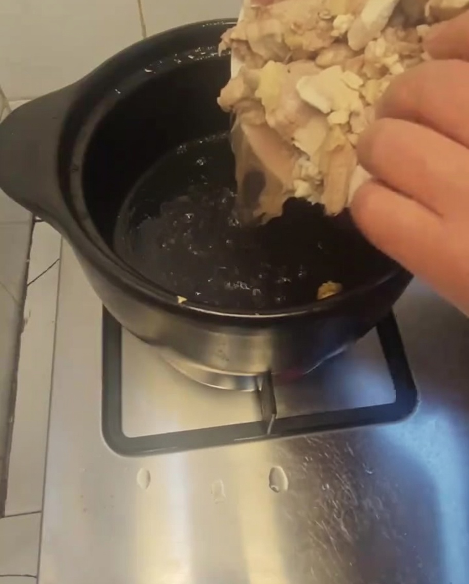 Blanchierte Hühnerstücke werden von einem weißen Teller in einen dunklen, vorgeheizten Tontopf gegeben.