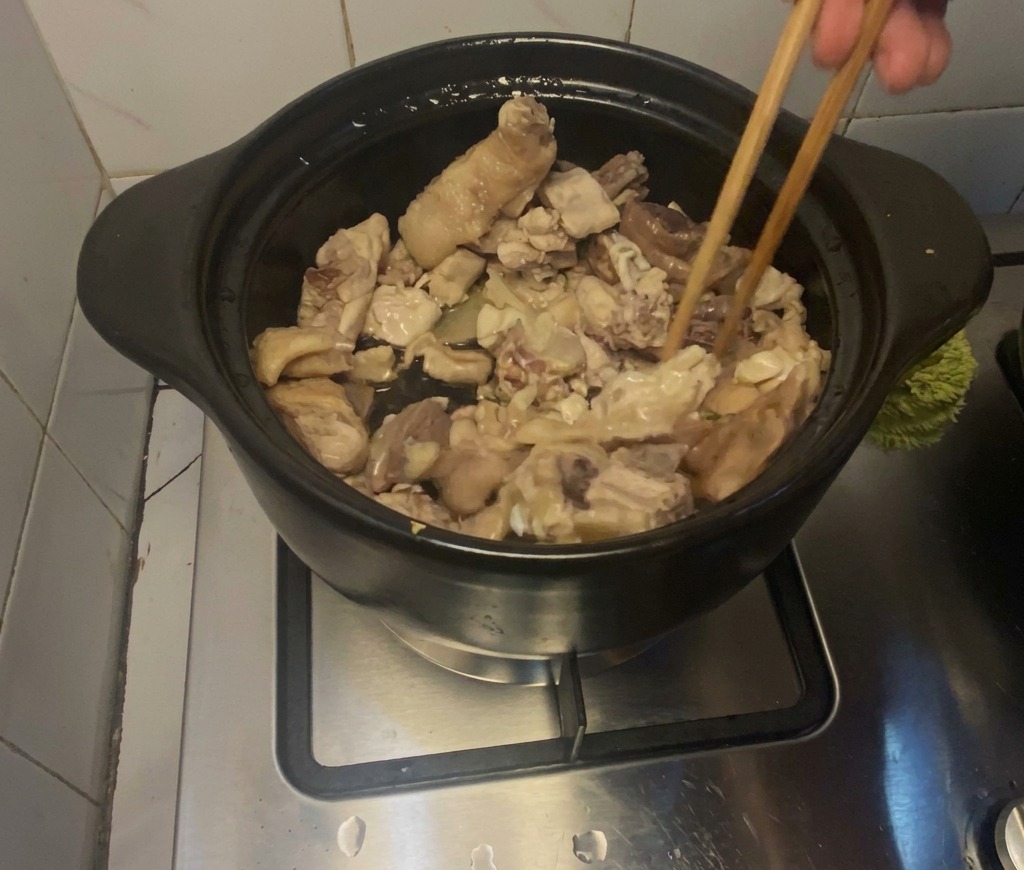 Hühnerstücke werden mit Holzstäbchen in einem schwarzen Tontopf auf dem Herd angebraten.