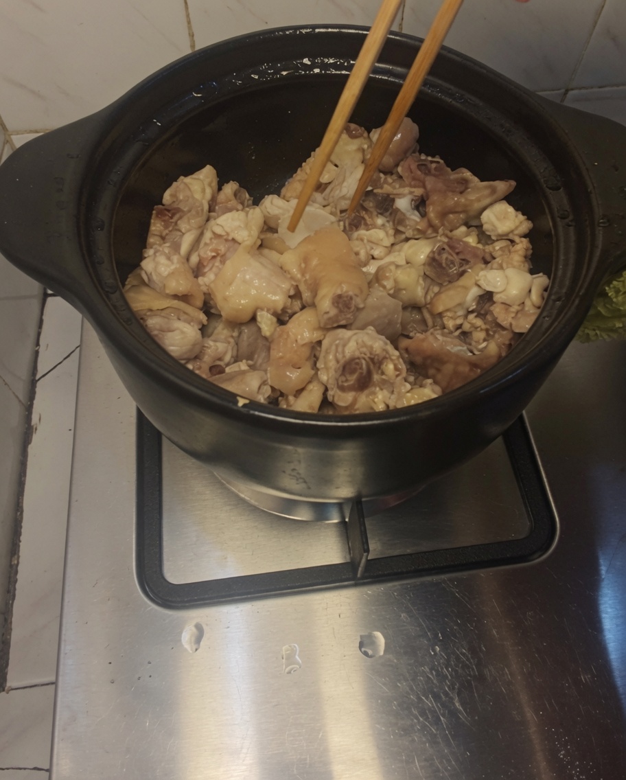 Holzstäbchen rühren Hühnerfleisch und Ingwerscheiben in einem erhitzten Tontopf um.