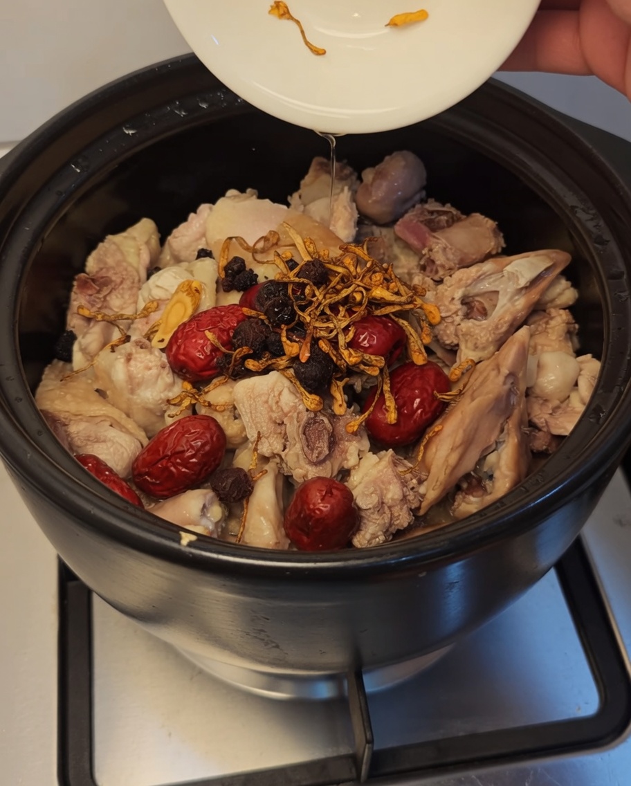 Cordyceps-Blüten, dunkle Goji-Beeren und Longan werden zum Huhn und den Datteln in den Tontopf gegeben.