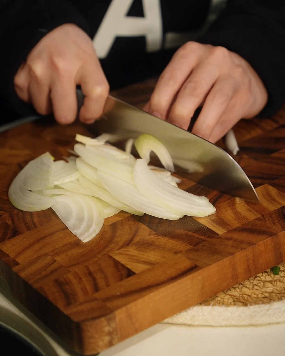 Dünn geschnittene weiße Zwiebelstreifen auf einem Holzschneidebrett.
