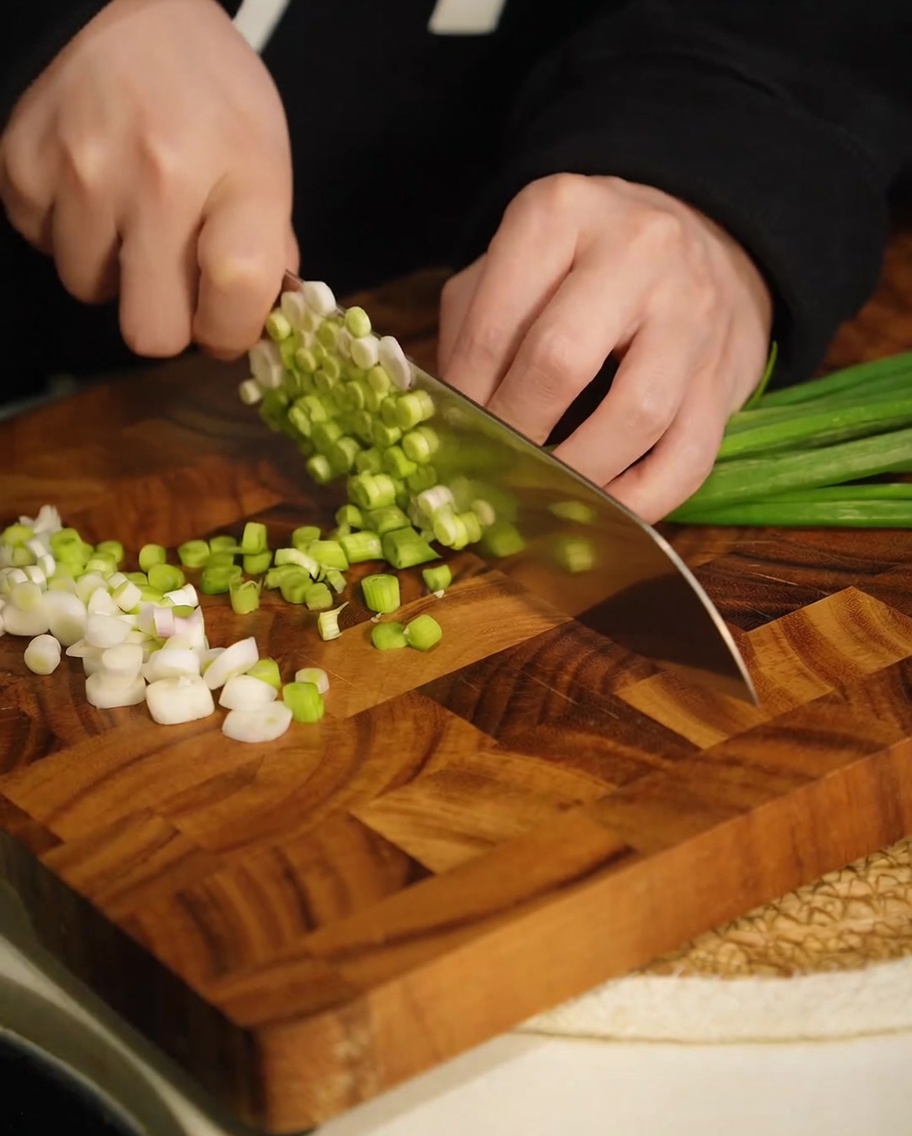 Frisch gehackte grüne Frühlingszwiebeln auf einem Holzbrett.