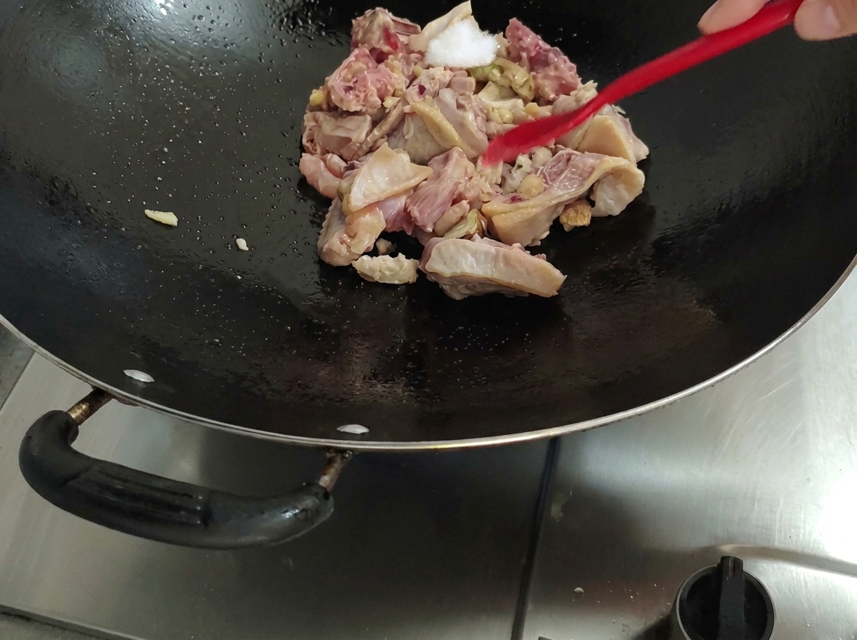 Mit einem roten Pfannenwender wird Salz zum Hähnchen im Wok gegeben.