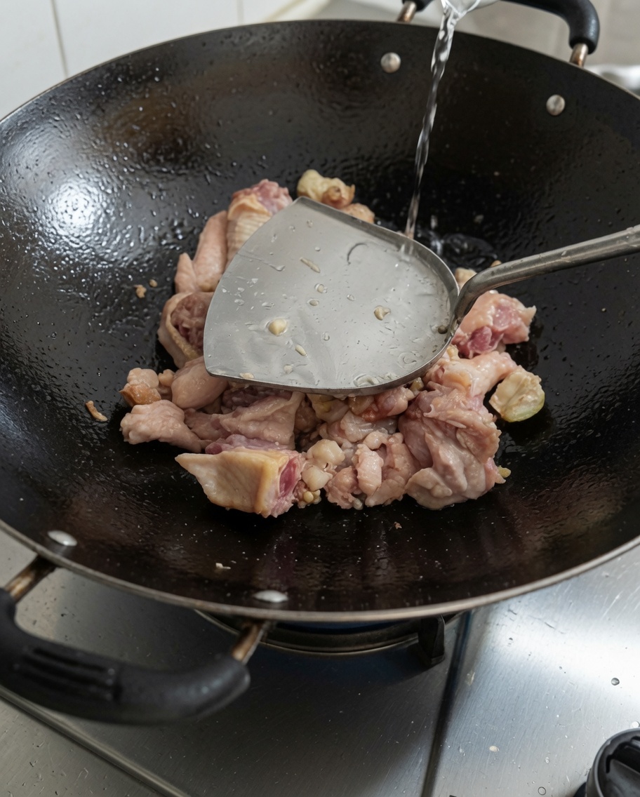 Frisches Wasser wird in den Wok mit dem angebratenen Hähnchen gegossen.