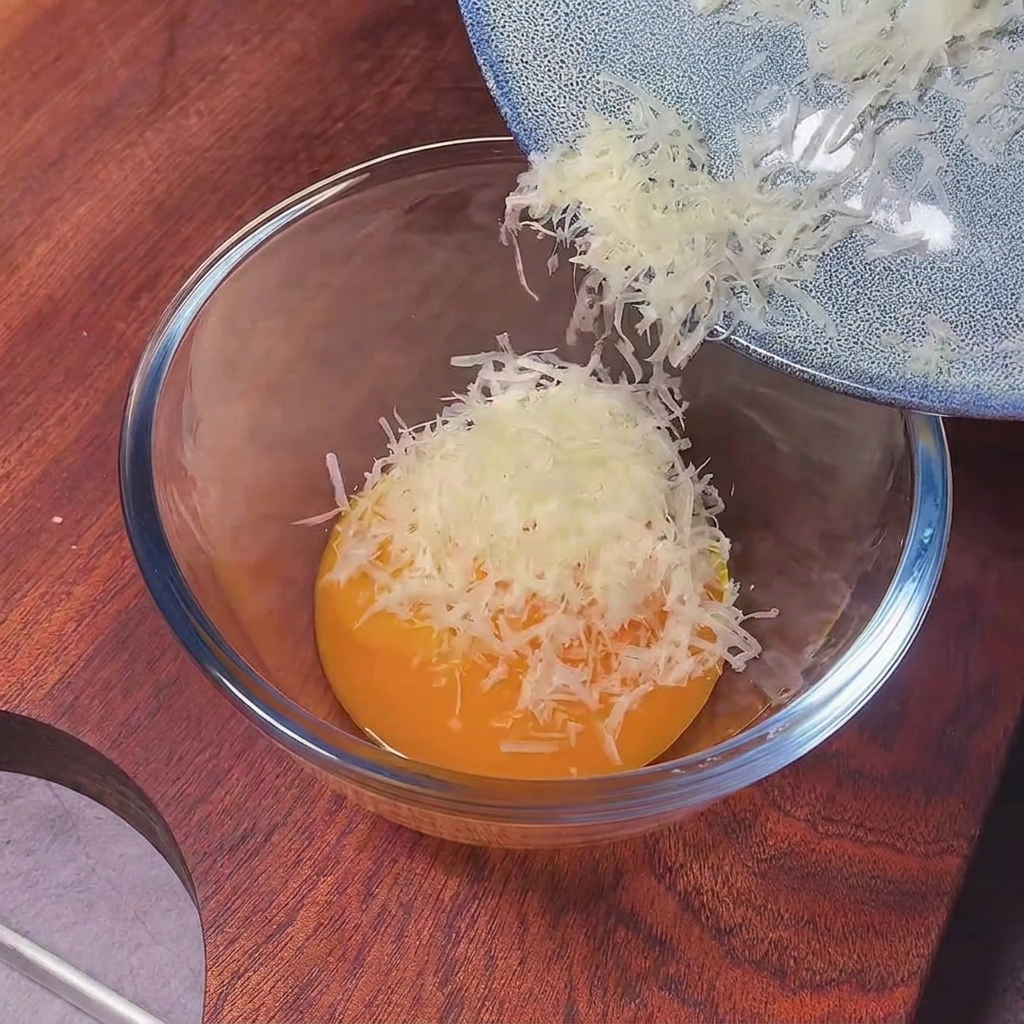 Frisch gemahlener schwarzer Pfeffer wird mit einem Löffel in die Ei-Käse-Basis eingerührt.