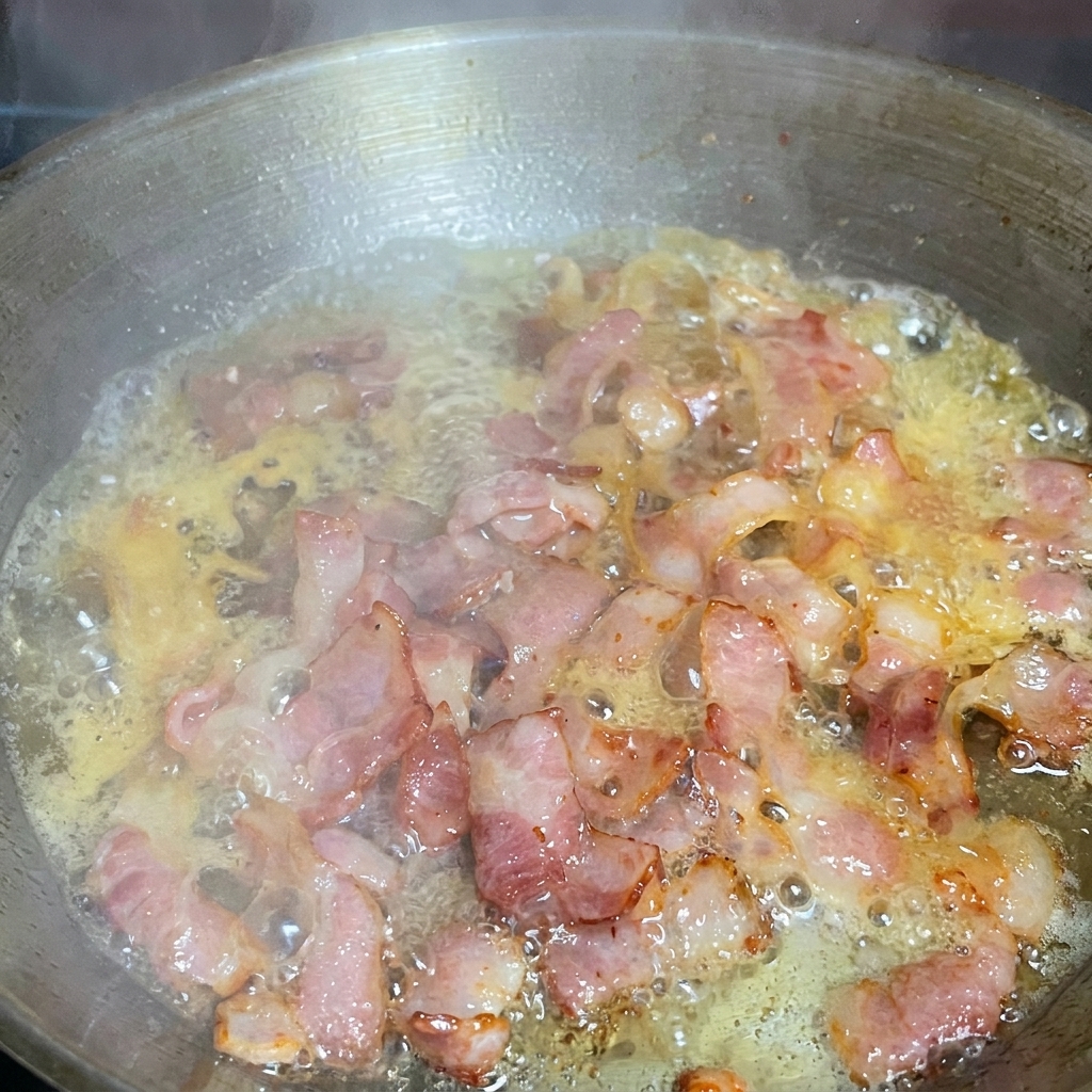 Spaghetti werden in der Pfanne mit gebratenem Speck und einem Spritzer Nudelwasser geschwenkt.