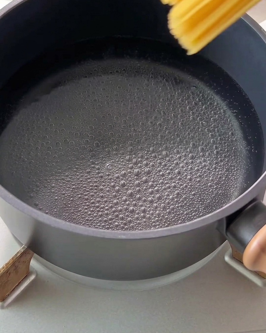 Spaghetti werden in einen Topf mit sprudelnd kochendem Wasser gegeben.