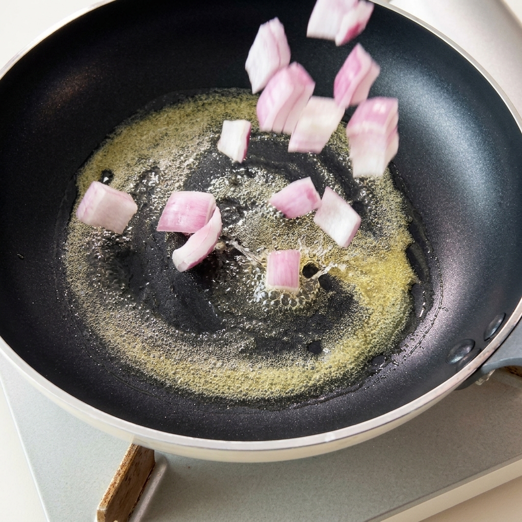 Gehackte rote Zwiebeln fallen in eine heiße Pfanne mit schäumender Butter.