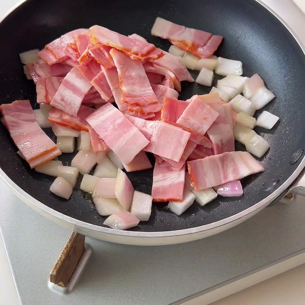 Gehackter Speck und gewürfelte Zwiebeln in einer trockenen Pfanne.