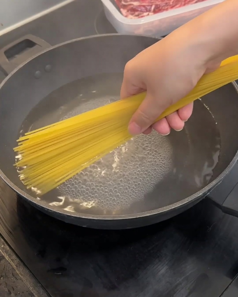 Trockene Spaghetti werden in einen Wok mit kochendem Wasser gegeben.
