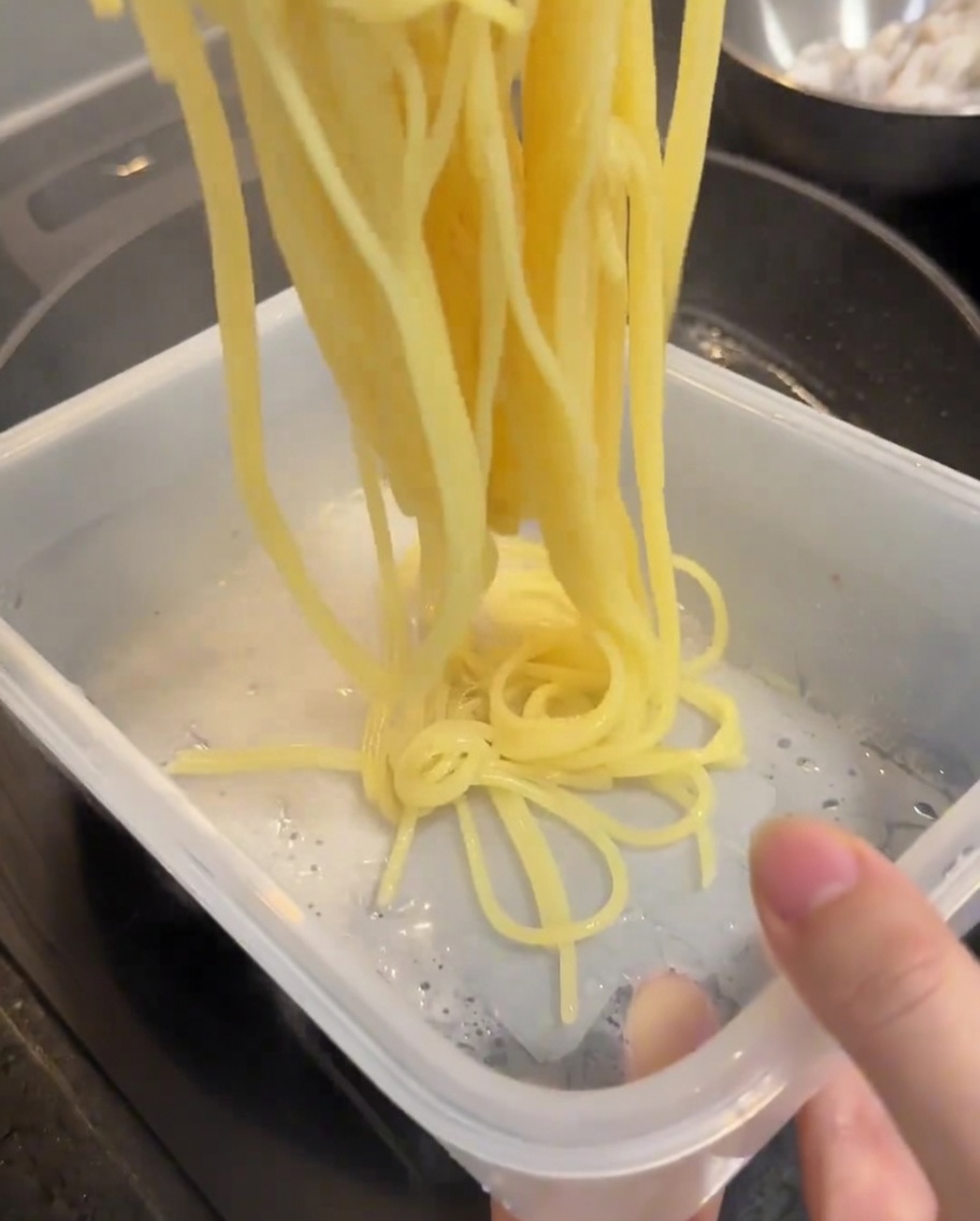 Gekochte Spaghetti werden aus dem Topf genommen und in einen Behälter mit kaltem Wasser gegeben.