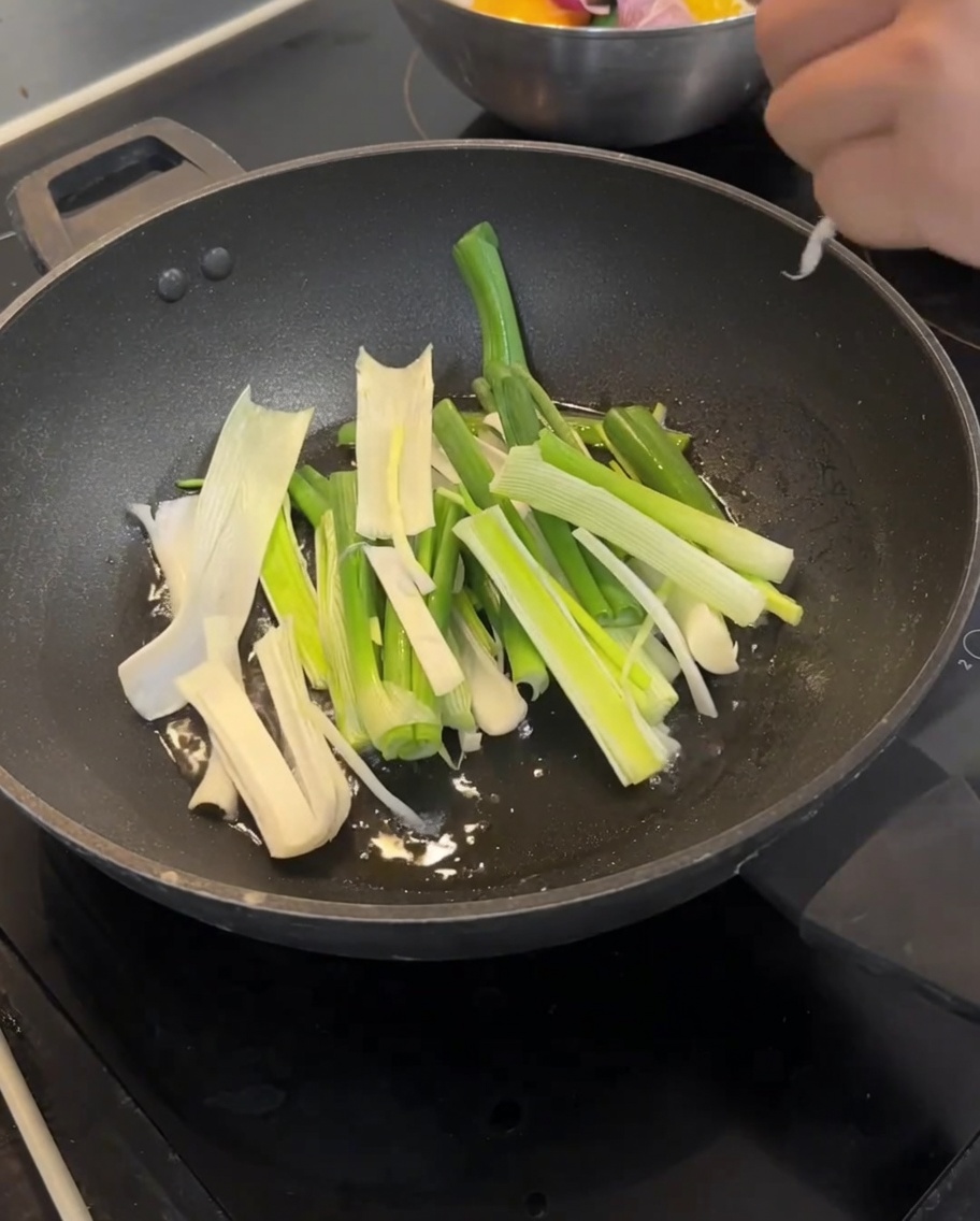 Grüne Frühlingszwiebelstücke braten in heißem Öl im Wok, bis sie goldbraun sind.