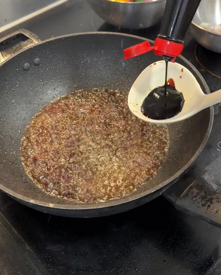 Dunkle Sojasauce wird aus einer Schöpfkelle in eine Pfanne mit Frühlingszwiebelöl gegossen.