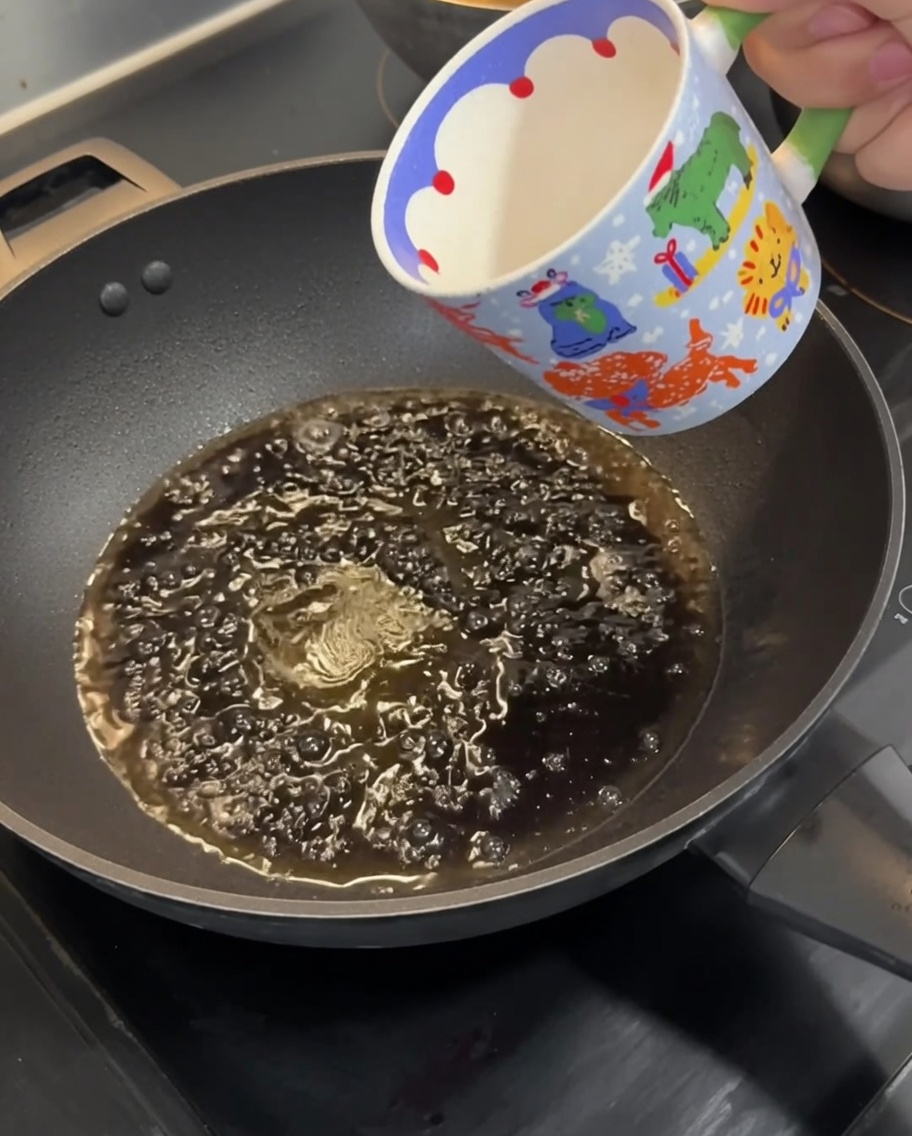 Eine Kelle rührt eine dunkle, köchelnde Saucenmischung in einer Pfanne.