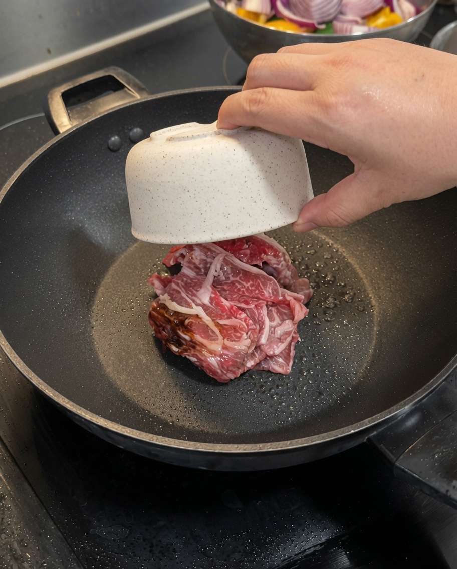 Dünn geschnittene rohe Rindfleischstücke braten in einer heißen Pfanne.