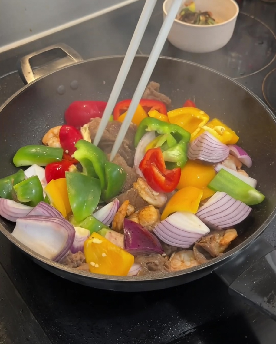 Bunte Paprika und rote Zwiebeln werden in den Wok zum Fleisch gegeben.