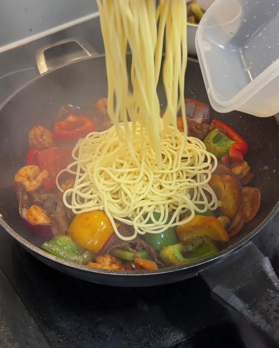 Gekochte Spaghetti werden in den Wok zu Fleisch und Gemüse gegeben.