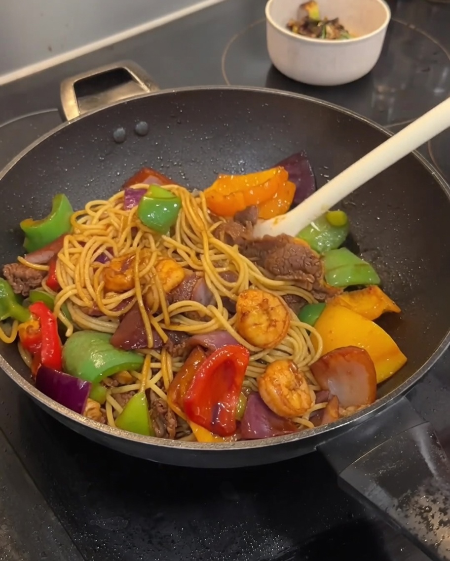 Nudeln werden mit Fleisch und Gemüse im Wok vermischt.