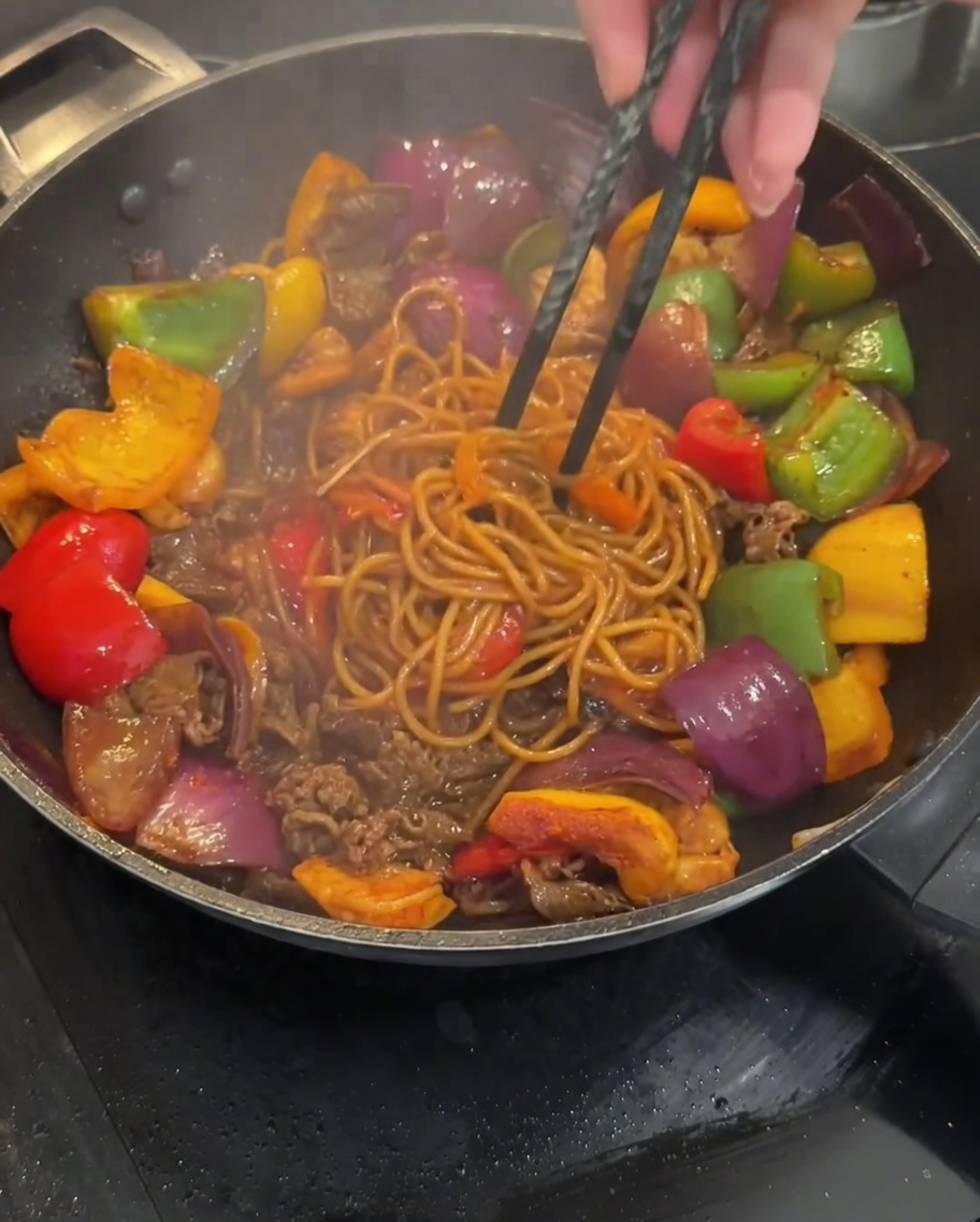 Die Nudelmischung wird im Wok gebraten, bis die Sauce vollständig aufgenommen ist.