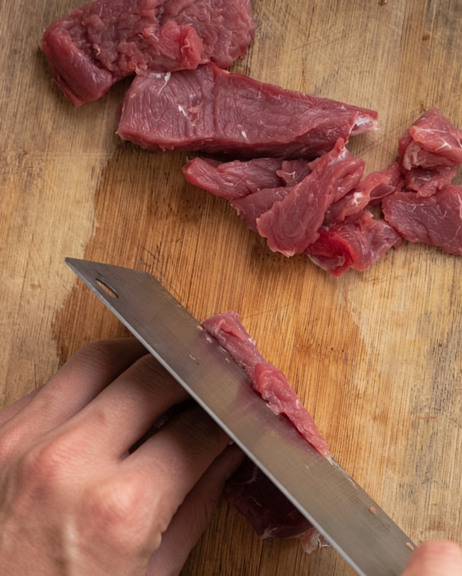 Rinderfilet wird auf einem Holzbrett in gleichmäßige, dünne Streifen geschnitten.