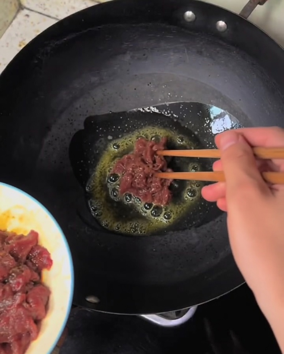 Rindfleischstreifen braten in einem heißen Wok und zeigen erste Bräunungsspuren.