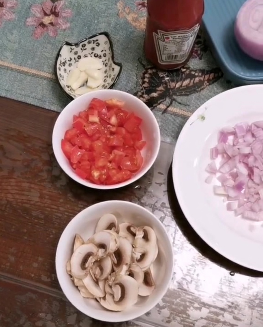 Eine Schüssel mit frisch gehackten Tomaten, geschnittenen Champignons und gehacktem Knoblauch auf einem Tisch.