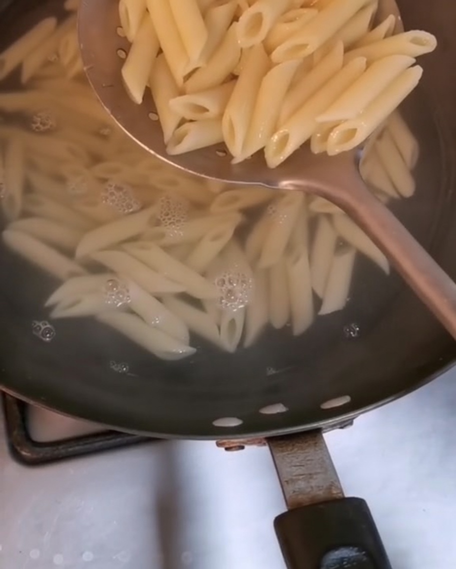 Penne-Nudeln werden mit einem großen Schaumlöffel aus kochendem Wasser gehoben.