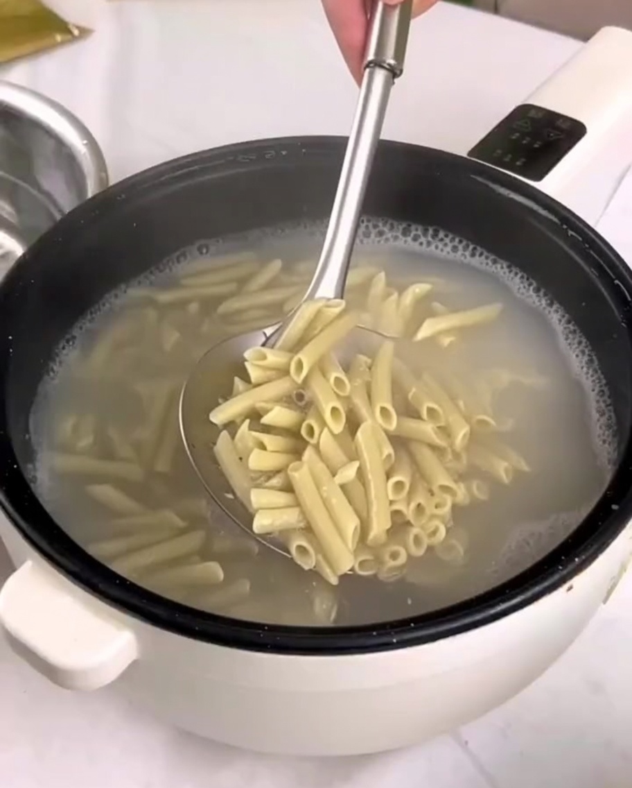 Gekochte Penne-Pasta wird mit einem Schaumlöffel in eine Schüssel mit kaltem Wasser gegeben.