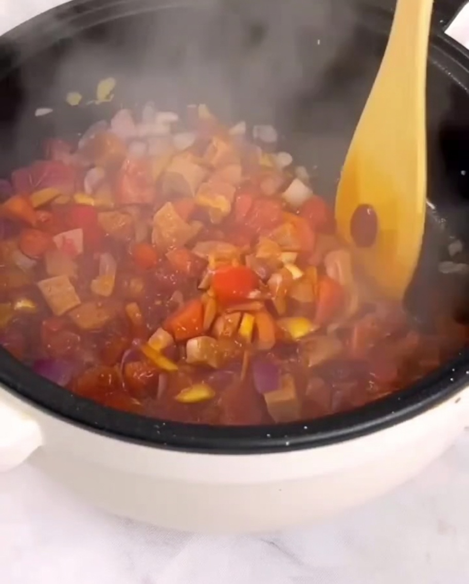 Gewürfelte Tomaten, Schinken und Gemüse werden mit einem Holzspatel in der Pfanne angebraten.