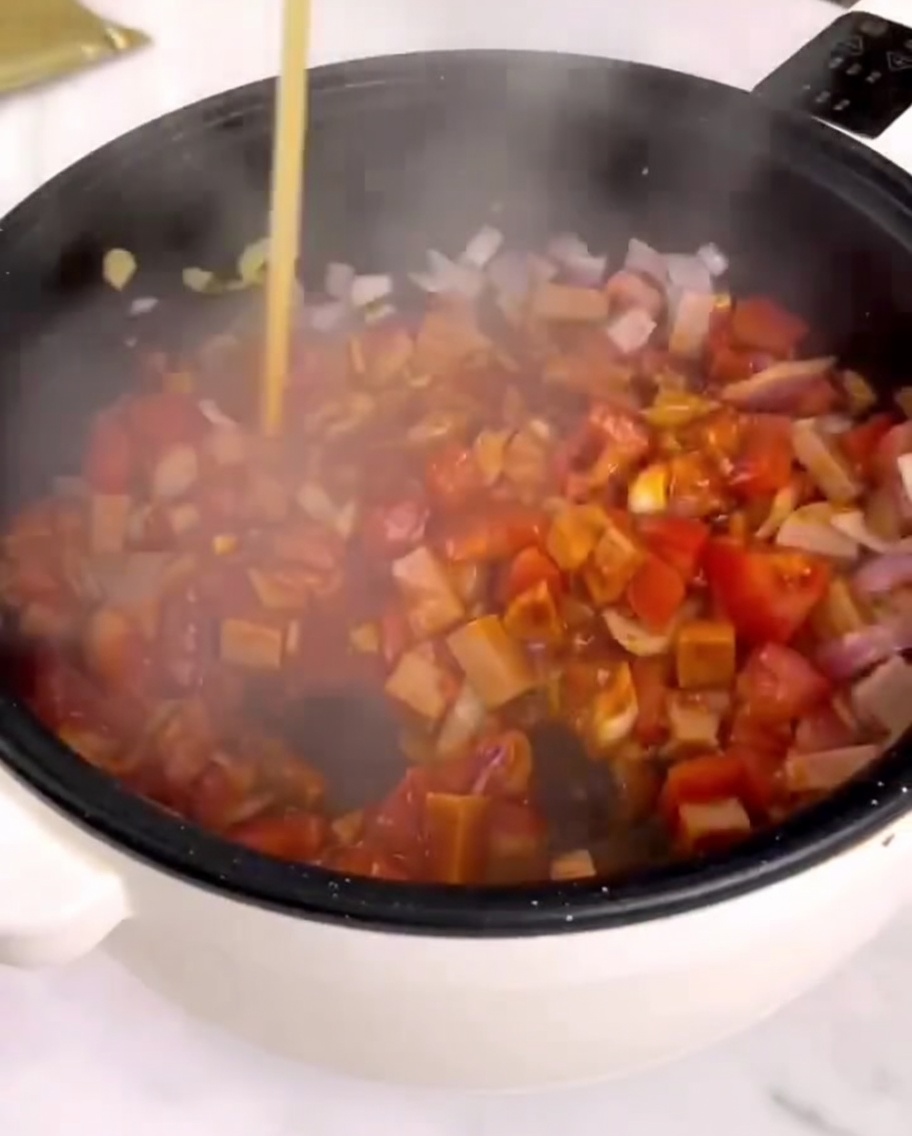 Pastasauce wird in eine Pfanne mit angebratenem Gemüse und Schinken gegeben.