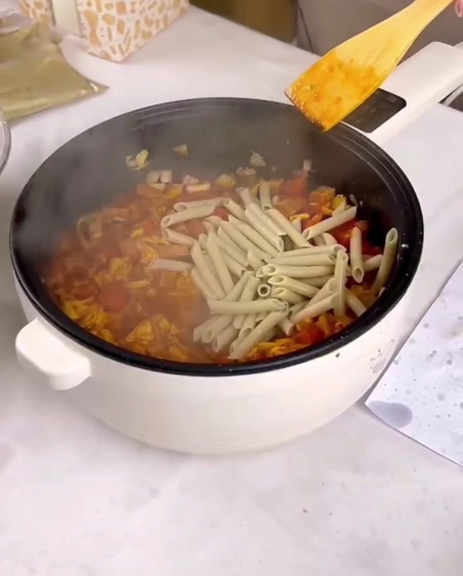 Gekochte Penne-Pasta wird in die Pfanne mit der Sauce und dem restlichen Inhalt gegeben.