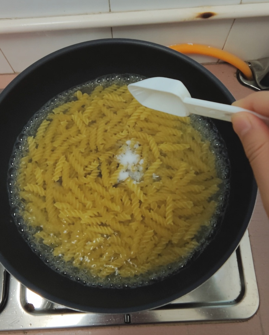 Ein Löffel Salz wird in einen Topf mit kochendem Nudelwasser gegeben.