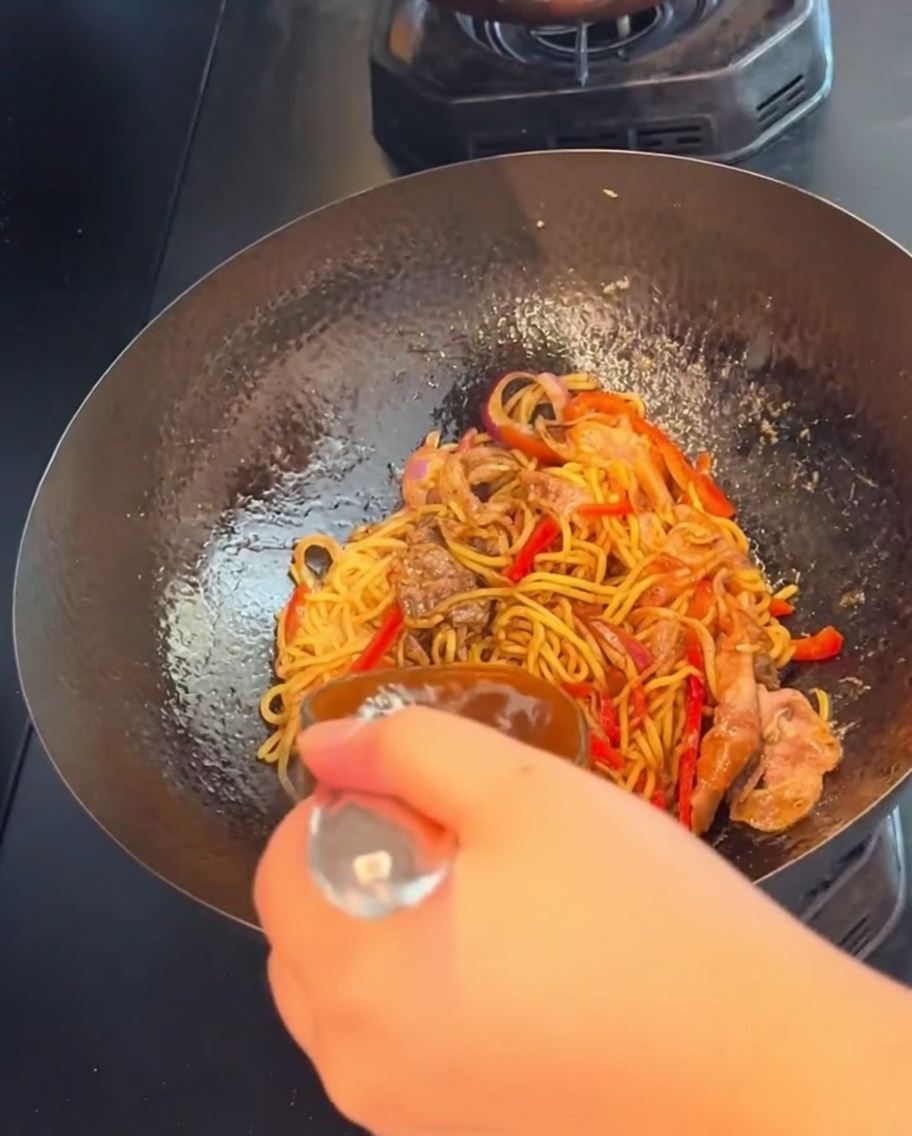 Eine Hand schwenkt und rührt die Spaghetti mit Rindfleisch bei starker Hitze im Wok.