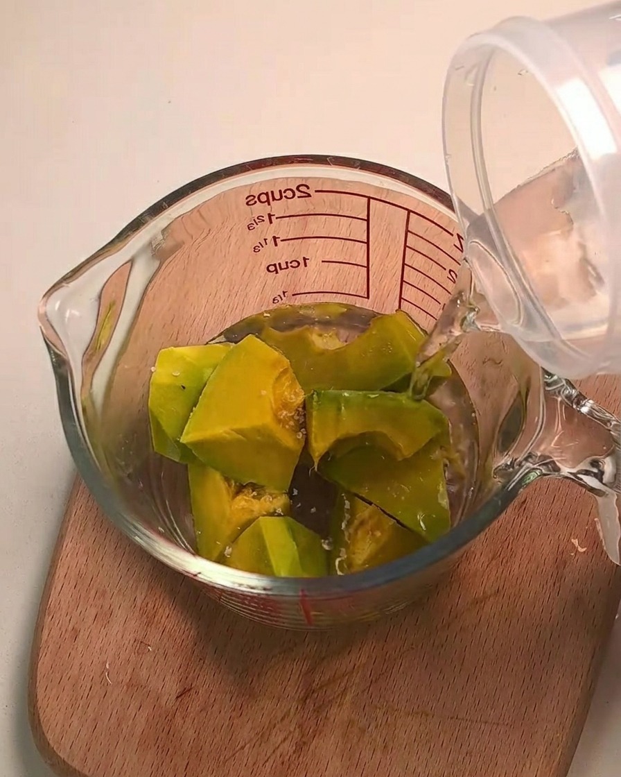 Wasser wird über Kabocha-Kürbisstücke in einem Glasmessbecher gegossen.