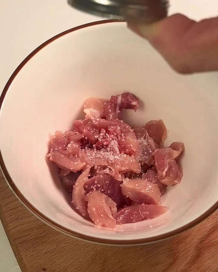 Hähnchenkeulenfleisch wird in einer weißen Schüssel mit Salz und Zitronensaft gewürzt.