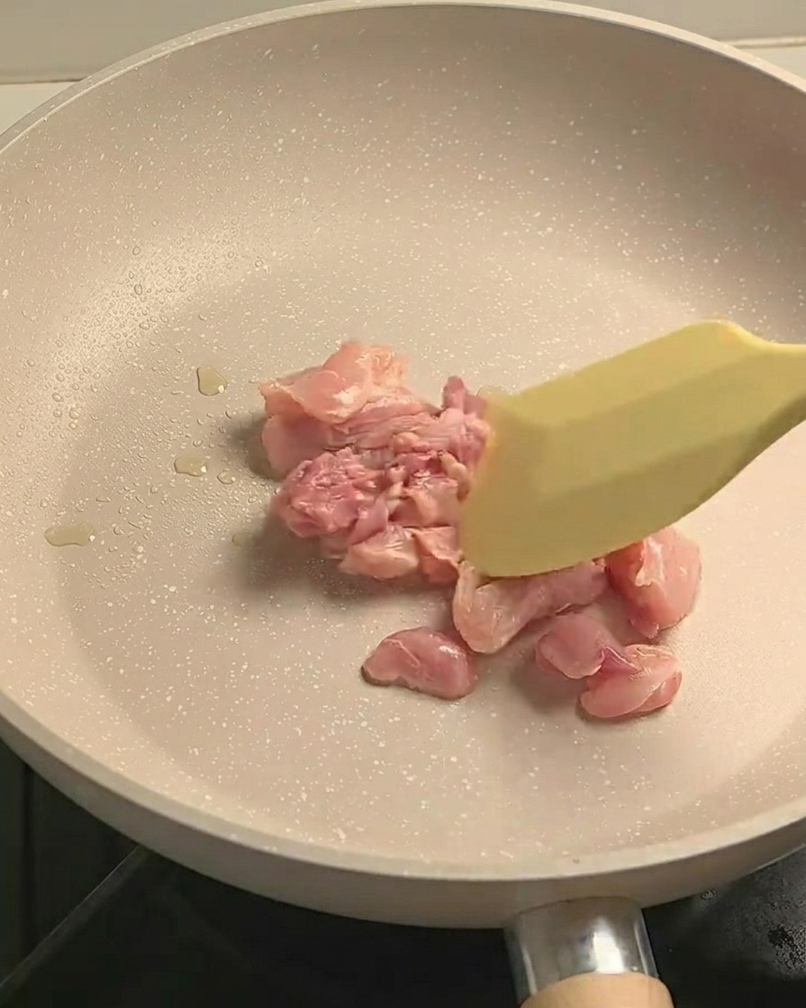 Gewürztes Hähnchenkeulenfleisch wird in einer beschichteten Pfanne angebraten und zeigt leichte Bräunung.