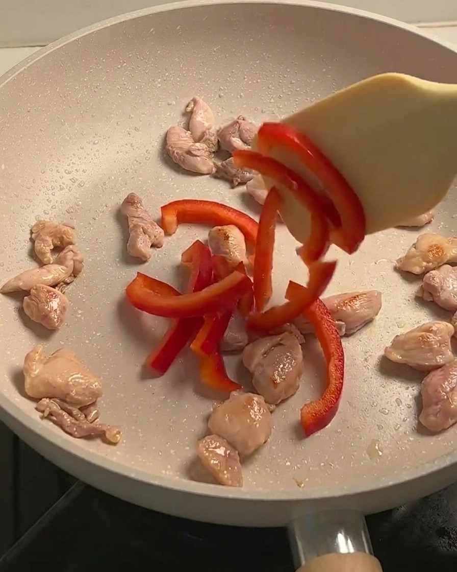 Angebratenes Hähnchen, geschnittene rote Paprika und Pilze schmoren gemeinsam in einer Pfanne.