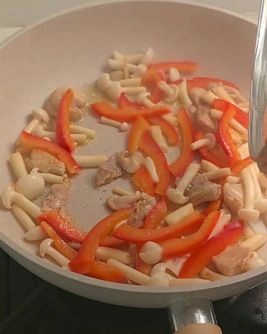 Gekochte Fusilli Pasta wird in die Pfanne mit der Hähnchen-Gemüse-Mischung gegeben.