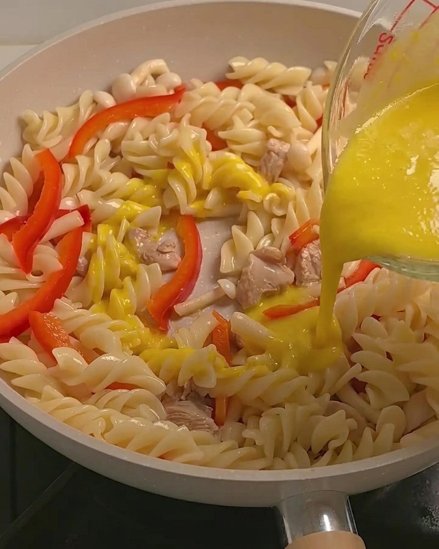 Cremige gelbe Kürbis-Sauce wird über Fusilli Pasta, Hähnchen und Gemüse in einer Pfanne gegossen.