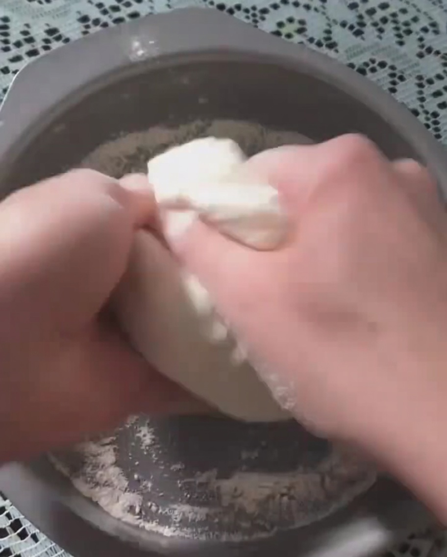 Hände drücken den fermentierten Pizzateig in eine runde Backform aus Metall.
