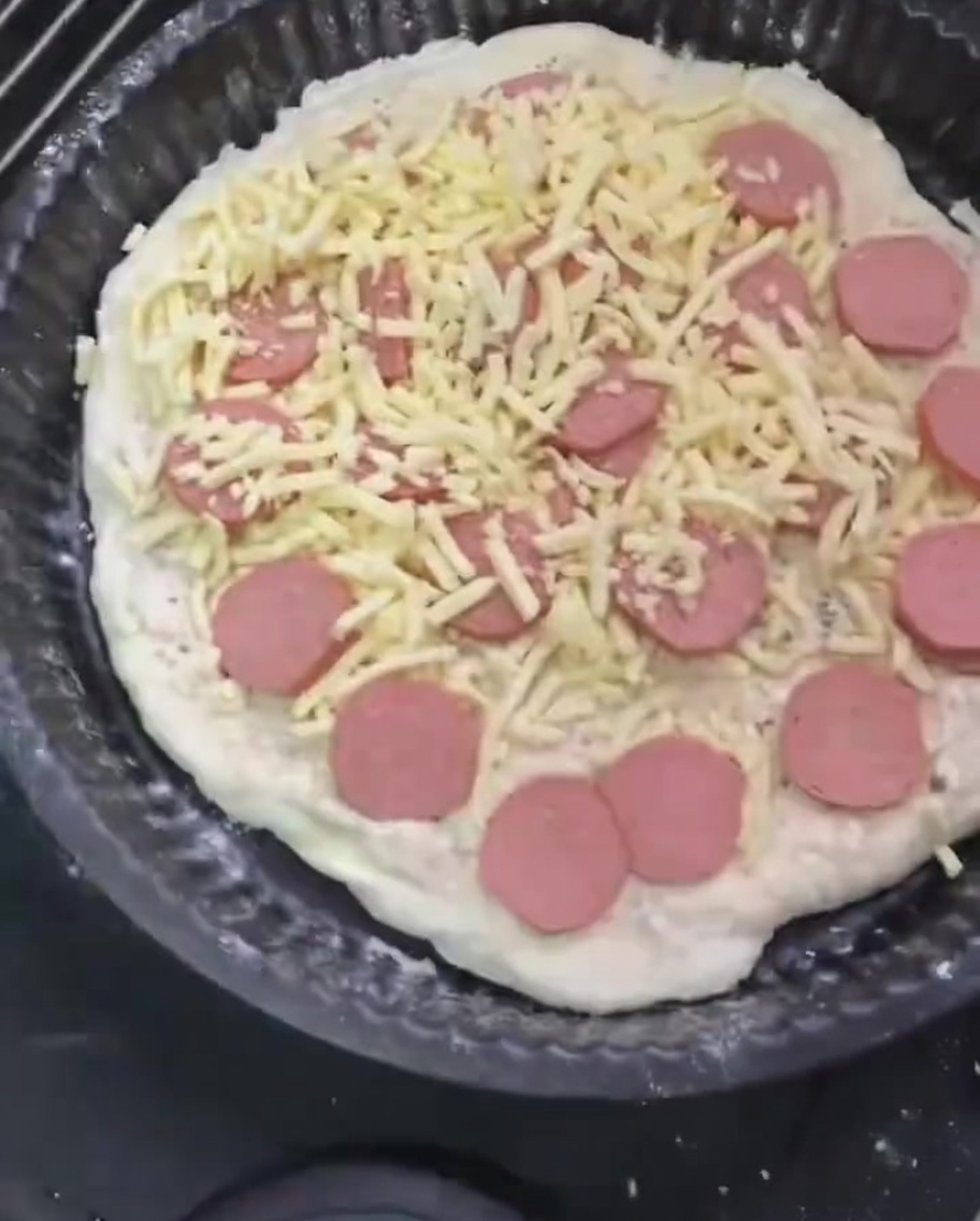 Eine abschließende Schicht geriebener Mozzarella wird über der belegten Pizza verteilt.