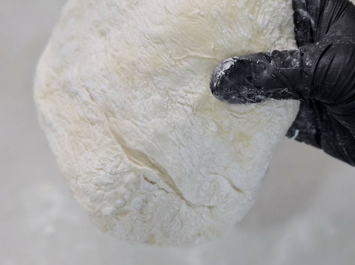 Pizzateig wird auf einer mit Maisgrieß bestäubten Arbeitsfläche flach gedrückt und auseinandergezogen.