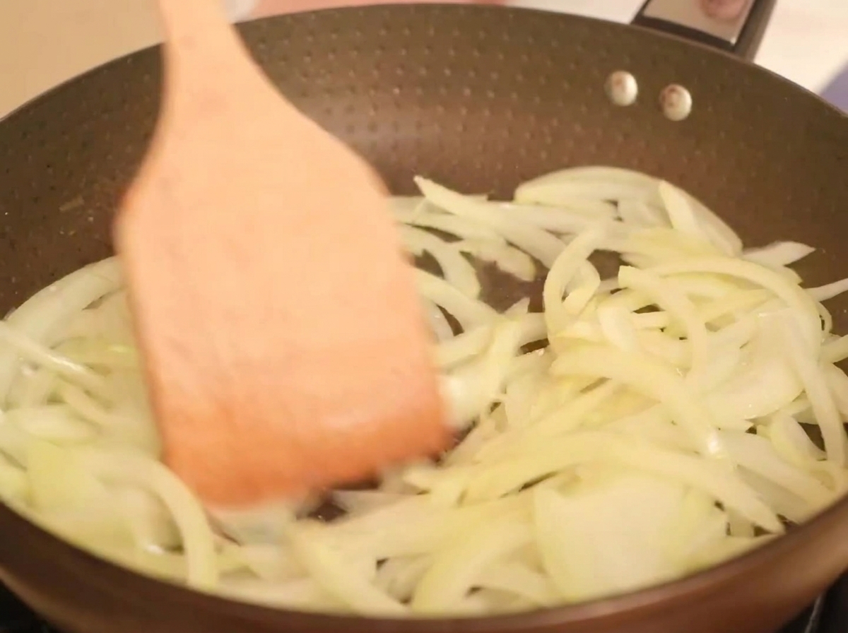 Zwiebelstreifen braten in einer heißen Pfanne mit Öl und werden mit einem Holzspatel gewendet.