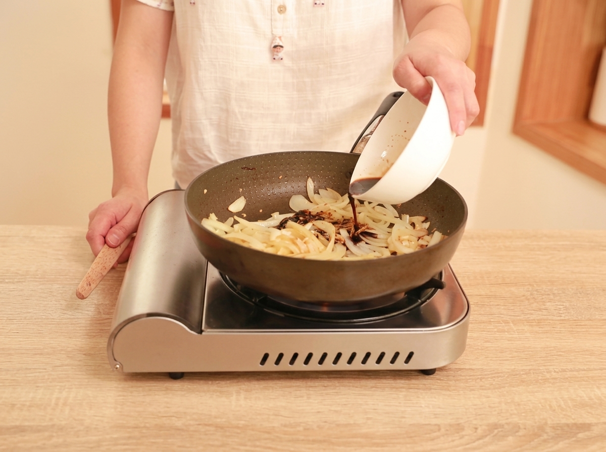 Dunkelbraune Sauce wird aus einer weißen Schüssel in eine Pfanne mit Zwiebeln, Ingwer und Knoblauch gegossen.