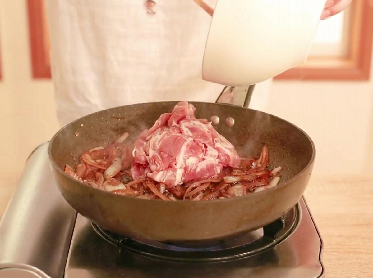 Rohes, dünn geschnittenes Rindfleisch wird in eine Pfanne mit dunkler Sauce und Zwiebeln gegeben, bereit zum Pfannenrühren.