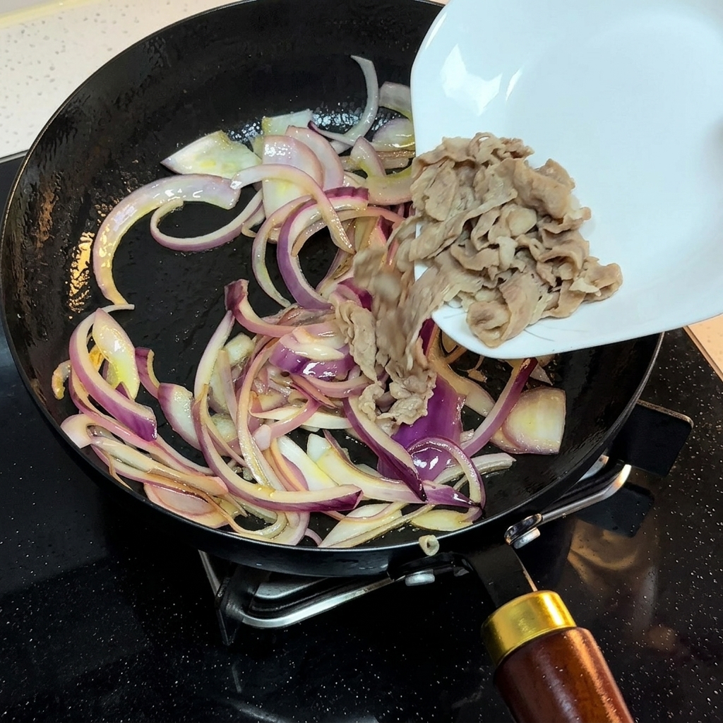 Blanchierte Rindfleischscheiben werden von einem weißen Teller zu den angebratenen Zwiebelstreifen in die Pfanne gegeben.