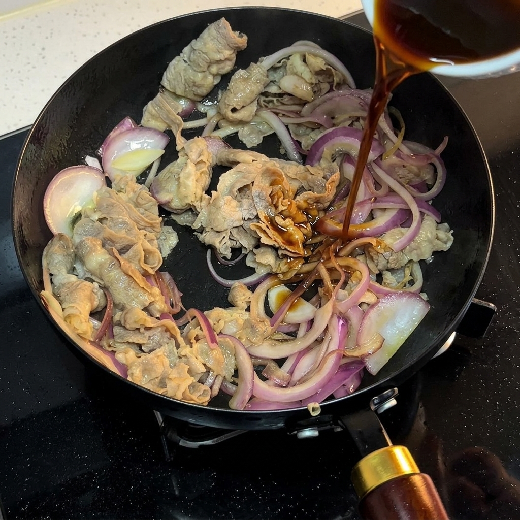 Eine dunkle Sauce wird aus einer kleinen Schüssel über das Rindfleisch und die Zwiebeln in der Pfanne gegossen.