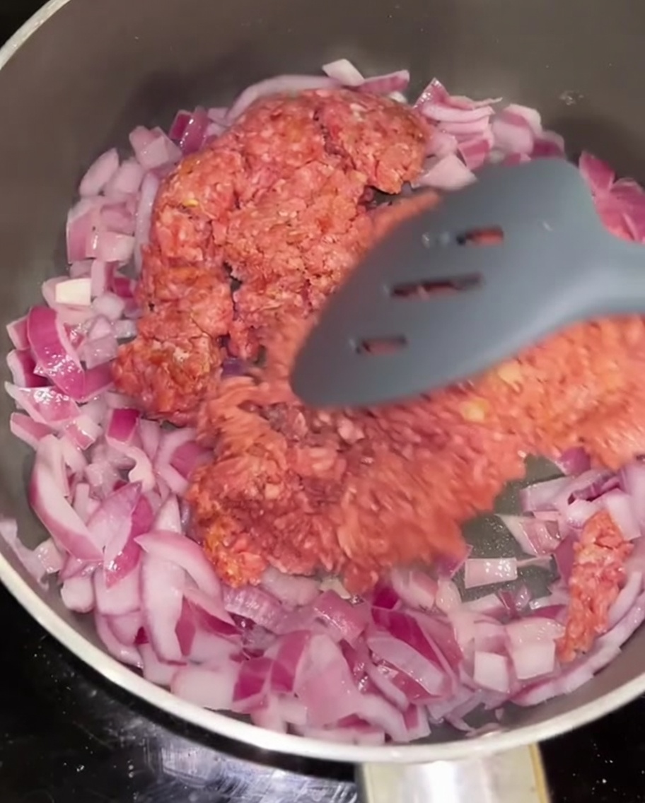 Rinderhackfleisch wird zusammen mit sautierten roten Zwiebeln in einer Pfanne angebraten.
